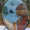 Beach hut with dolphins memorial glass suncatcher featuring ocean waves, palm tree, pier, and cremation ash fused into the glass in natural outdoor light