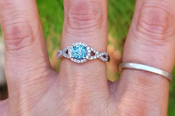 Infinity cremation ring with Blue Silver Crinkle glass set in a sterling silver halo band worn on hand in natural light