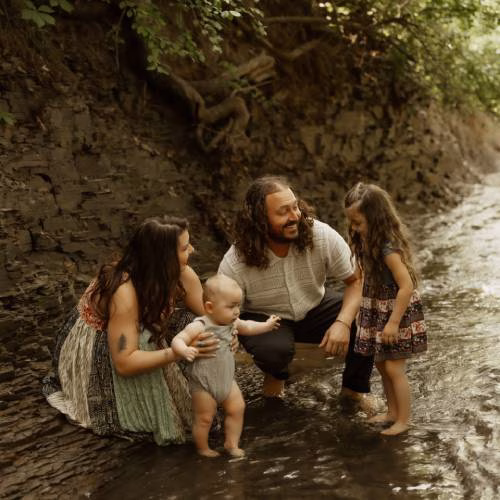 Glass artist with family standing together in a shallow creek outdoors