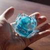 Memorial glass flower being held in hand showing blue glass tones and cremation ash suspended inside, by Sands of Time.