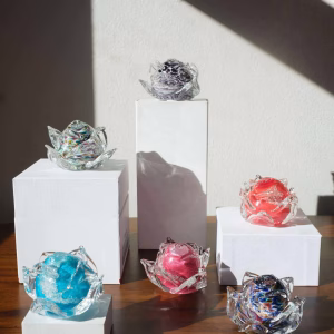 Display of multiple memorial glass flowers in different color variations arranged on staggered pedestals, by Sands of Time.