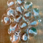 Multiple Heaven Drop memorial glass pieces displayed on a wooden surface with cremation ash suspended inside, by Sands of Time.