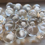 Multiple Heaven Drop memorial glass pieces displayed on a wooden surface with cremation ash suspended inside, by Sands of Time.