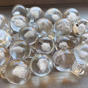Multiple Heaven Drop memorial glass pieces displayed on a wooden surface with cremation ash suspended inside, by Sands of Time.