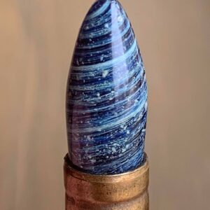 A close up of shot of a memorial glass bullet tip with white cremation ash set inside a brass casing.
