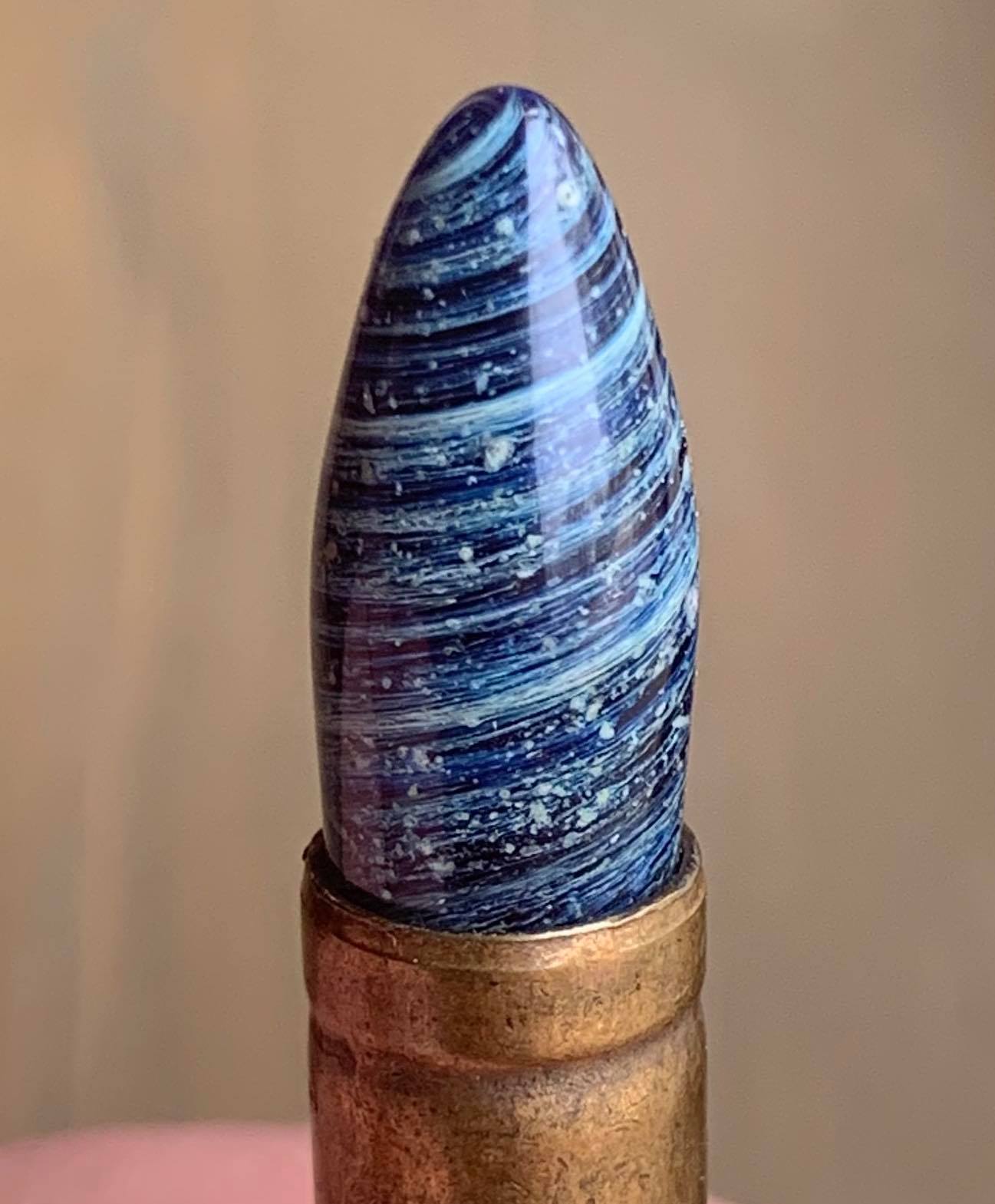 A close up of shot of a memorial glass bullet tip with white cremation ash set inside a brass casing.