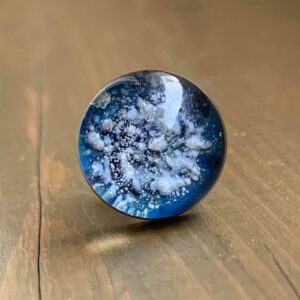 A blue colored glass memorial hat-pin sits on a wooden surface.