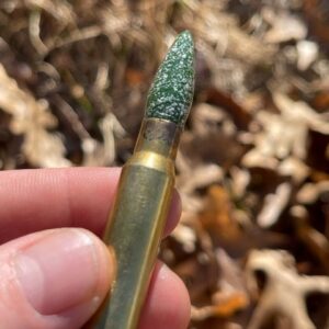 A memorial glass bullet tip with white cremation ash set inside a brass casing held in hand outdoors.