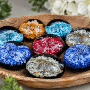 Elegant display of handcrafted memorial comfort stones by Sands of Time featuring thumb-groove glass touchstones with vibrant blue, turquoise, red, amber, and lavender floral designs on black backgrounds.