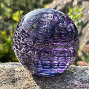 Amethyst birthstone glass paperweight with cremation ashes in a Ripple Vortex design, shown outdoors in natural light
