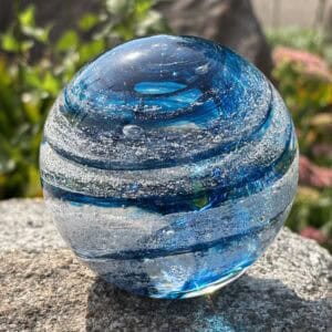 Aquamarine birthstone glass paperweight with cremation ashes in a Sparkle Swirl design, shown from a second angle outdoors