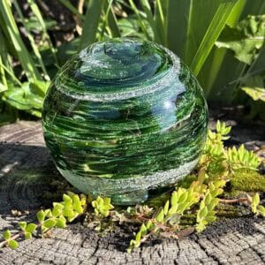 Emerald birthstone glass paperweight with cremation ashes in a Sparkle Swirl design, shown outdoors in natural light