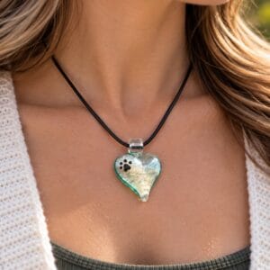 Woman wearing a heart-shaped paw print glass cremation pendant with pet ashes on a black cord