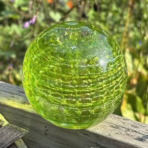 Peridot birthstone glass paperweight with cremation ashes in a Ripple Vortex design, shown outdoors in natural light