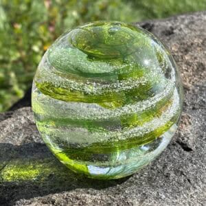 Peridot birthstone glass paperweight with cremation ashes in a Sparkle Swirl design, shown outdoors in natural light