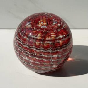 Ruby birthstone glass paperweight with cremation ashes in a Ripple Vortex design, shown in natural light