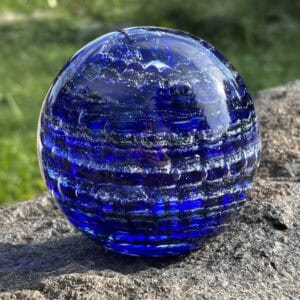 Front view of sapphire blue birthstone glass paperweight with cremation ashes in a Ripple Vortex design
