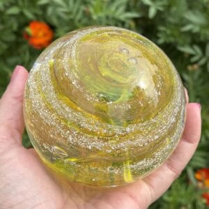 Handheld angled top view of yellow topaz birthstone glass paperweight with cremation ashes in a Gold Sparkle Swirl design
