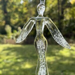 Clear glass angel memorial suncatcher with cremation ashes visible in the wings and body hanging outdoors