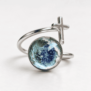 Blue glass cross cremation ring with ashes encased inside a handmade glass jewel and sterling silver wrap-around band